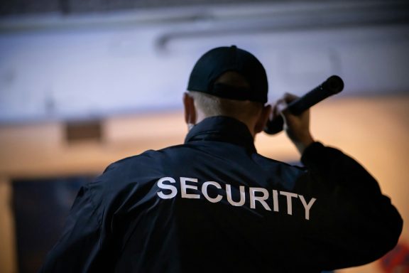 Sicherheitskraft mit Mikrofon, Rückenansicht, trägt Jacke mit der Aufschrift "SECURITY".